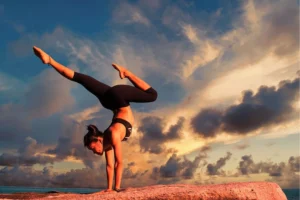 Athlete performing a handstand on a rocky ledge beneath a dramatic blue and golden sunset sky.