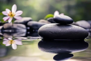 Smooth black zen stones beside pale flowers reflected in calm water.