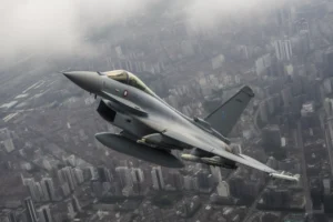 Modern grey fighter jet banking above a dense cityscape seen through atmospheric haze.